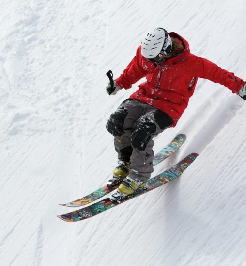 A skier in a red jacket descends a steep snowy slope, showcasing skill and adventure in winter sports.